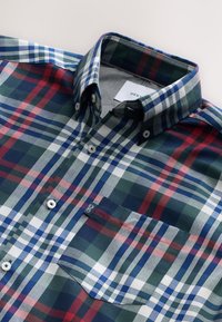 Chemise à carreaux vert, bleu marine, rouge et blanc. Dotée d'un col boutonné, d'une poche poitrine et de boutons blancs. Texture de tissu douce.