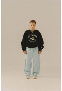Sudadera negra con gráfico de "THE SWARM", combinada con pantalones deportivos sueltos de color azul claro. Presenta detalles dorados y una silueta relajada.