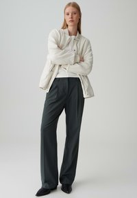 Weiße Bomberjacke, graue weite Hose und schwarze spitz zulaufende Schuhe. Glatte Textur und neutrale Farben mit minimalistischem Design.