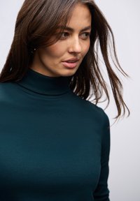 Tuurblauwe coltrui met een geribbelde textuur en een aansluitende pasvorm. De stof lijkt zacht en glad, met een minimalistisch ontwerp zonder zichtbare patronen of versieringen.