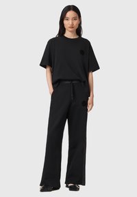 T-shirt nera oversize con maniche corte e scollatura rotonda, abbinata a pantaloni neri a gamba larga con bottoni a pressione lungo le cuciture laterali.