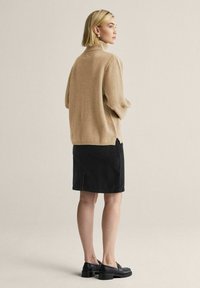 Beige polotröja med avslappnad passform, kombinerad med en svart kjol. Outfiten har en sidospalt och svarta kraftiga skor.