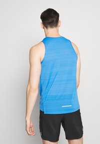 Blå ærmeløs sports skjorte med tekstureret stof, rund halsudskæring og reflekterende detalje bagpå, sammen med sorte shorts.