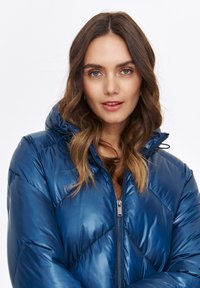 Padded blue jacket with a shiny finish, zippered front, and hood. Features a diamond quilt pattern and elastic cuffs for snug fit.