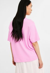 Tætsiddende lyserød bomulds T-shirt med korte ærmer, rund halsudskæring og en afslappet silhuet, vist fra ryggen.