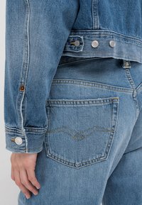 Ljusblå denimjacka med silverfärgade tryckknappar, två bakfickor med zigzagstygn och en avslappnad passform.
