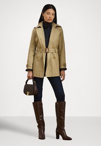 Trenci bej cu design cu două rânduri de nasturi, talie cu curea și epoleți; asortat cu blugi de culoare închisă și cizme maro din piele până la genunchi. Geantă maro.