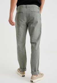 Spodnie w szaro-czarny wzór w zygzak, o luźnym kroju, z podwiniętymi mankietami i dwiema tylnymi kieszeniami, noszone z beżowymi sneakersami.