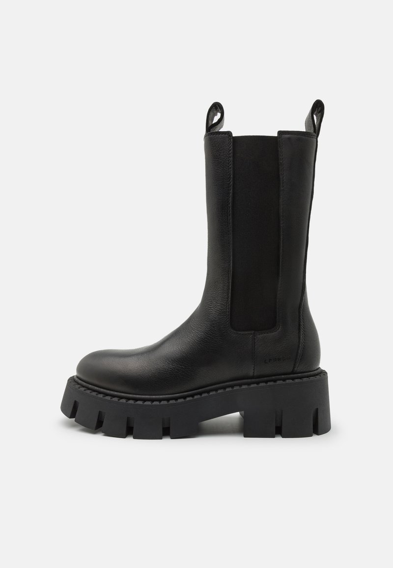 Bottines en cuir noir avec panneaux élastiques sur les côtés, languettes de tirage, semelle crantée épaisse et détails de couture renforcée. La surface a une texture lisse.