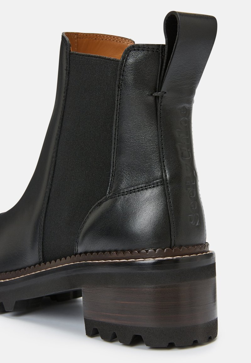 Bottes noires en cuir à cheville avec des panneaux latéraux en élastique, un dessus texturé, un talon épais foncé et un détail du logo embossé à l'arrière.