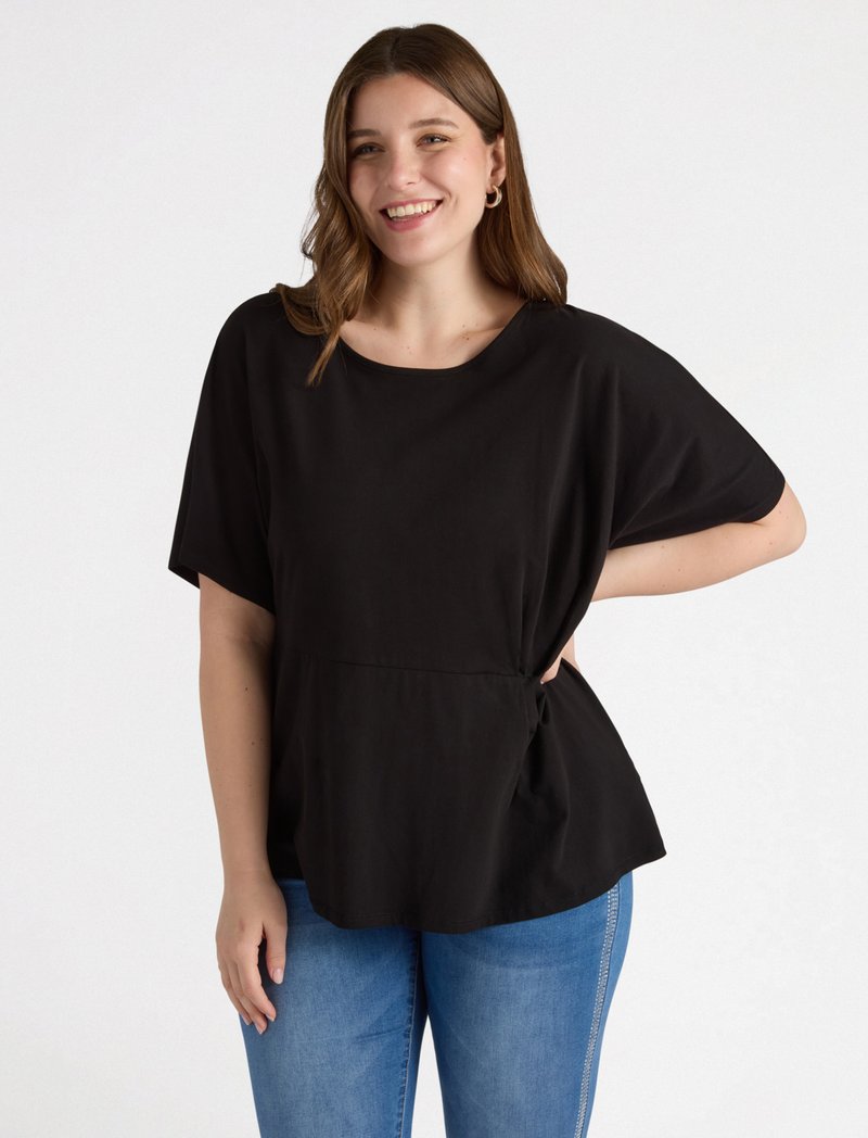 Schwarzes Oberteil mit lockerer Passform und kurzen Ärmeln, mit einem gerafften Taillendetail. Kombiniert mit hellblauen Jeans. Glatte Textur.
