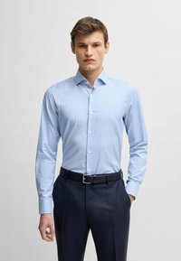 Jasnoniebieska koszula w kratę z bawełny, z długim rękawem, z kołnierzykiem zapinanym na guziki, zestawiona z ciemnymi spodniami i czarnym paskiem.