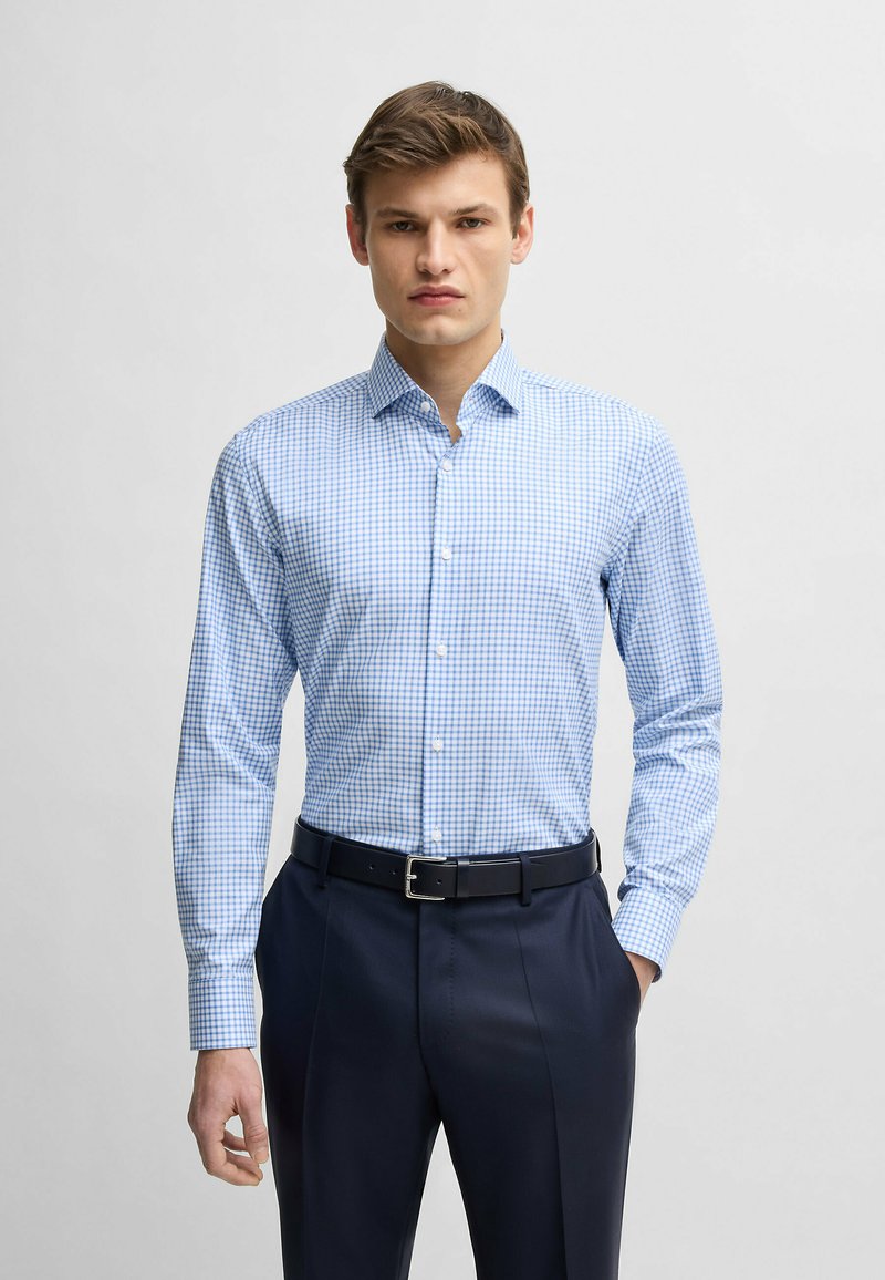 Jasnoniebieska koszula w kratę z bawełny, z długim rękawem, z kołnierzykiem zapinanym na guziki, zestawiona z ciemnymi spodniami i czarnym paskiem.