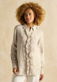 Ľahká pruhovaná košeľa v béžovej a krémovej farbe, s volánovým zapínaním a gombíkovým uzáverom. Dlhé rukávy s detailmi na manžetách.