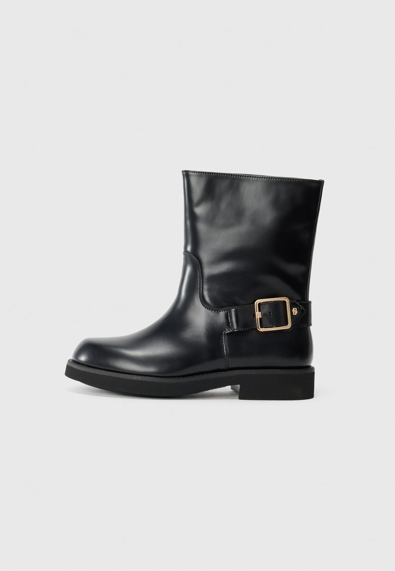 Black leather ankle boot with a smooth finish, curved toe, and a gold buckle accent on a leather strap, mounted on a flat rubber sole.