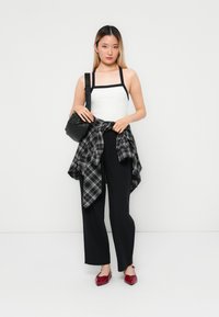 Hvit tanktopp med svarte stropper, svarte vidt bukser, rutete flanell skjorte rundt livet, og skinnende røde spisse sko. Svart crossover-veske.