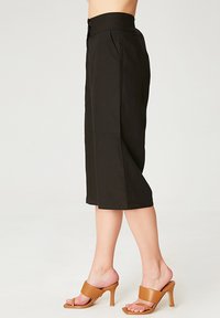 Culottes noires, de longueur genoux, en tissu léger, avec une taille haute, une fermeture à boutons et des poches latérales. Texture lisse et coupe ajustée.