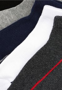 Cinq paires de chaussettes de couleurs variées : gris, marine, blanc et gris foncé, avec une accent rouge sur la paire gris foncé. Texture tricotée sur l'ensemble.