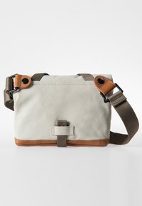Borsa a tracolla in tela grigio chiaro con dettagli in pelle marrone e una tracolla piatta. Presenta una chiusura a bottone e una base testurizzata.