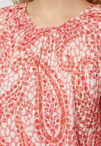 Leichte Bluse mit einem pink- und elfenbeinfarbenen, abstrakten Tierdruck. Faltentextur mit Rundhalsausschnitt und einem kleinen Knopfdetail.