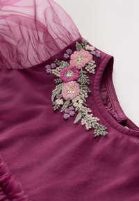 Lila klänning med broderade blommor i rosa, lavendel och grönt. Genomskinliga tyllärmar och texturerat tyg med volangdetalj längst ner.