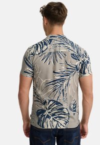 Camisa de manga corta en gris claro con estampado de hojas tropicales azules; textura suave; corte ajustado; detalle en la parte trasera; sin etiquetas visibles.