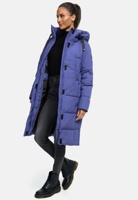 Puffer coat in vibrant purple, featuring a hood, black accents, and quilted texture. Paired with dark jeans and black lace-up boots.