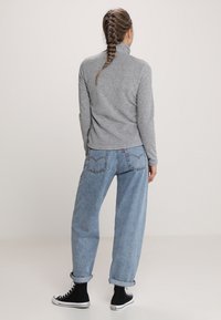 Szary polar z wysokim kołnierzem w zestawieniu z jasnoniebieskimi, luźnymi dżinsami. Całość uzupełniają czarne wysokie trampki.