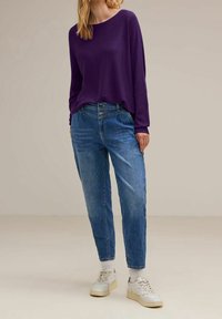 Lila långärmad topp kombinerad med ljusblå löst sittande jeans. Vita sneakers med beige sulor fulländar outfitet. Enkel design och avslappnad look.