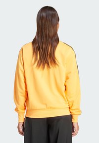 Gelbes Sweatshirt mit lockerer Passform, gerippten Bündchen und Saum sowie kontrastierenden schwarzen Seitenstreifen. Glatter, leichter Stoff.