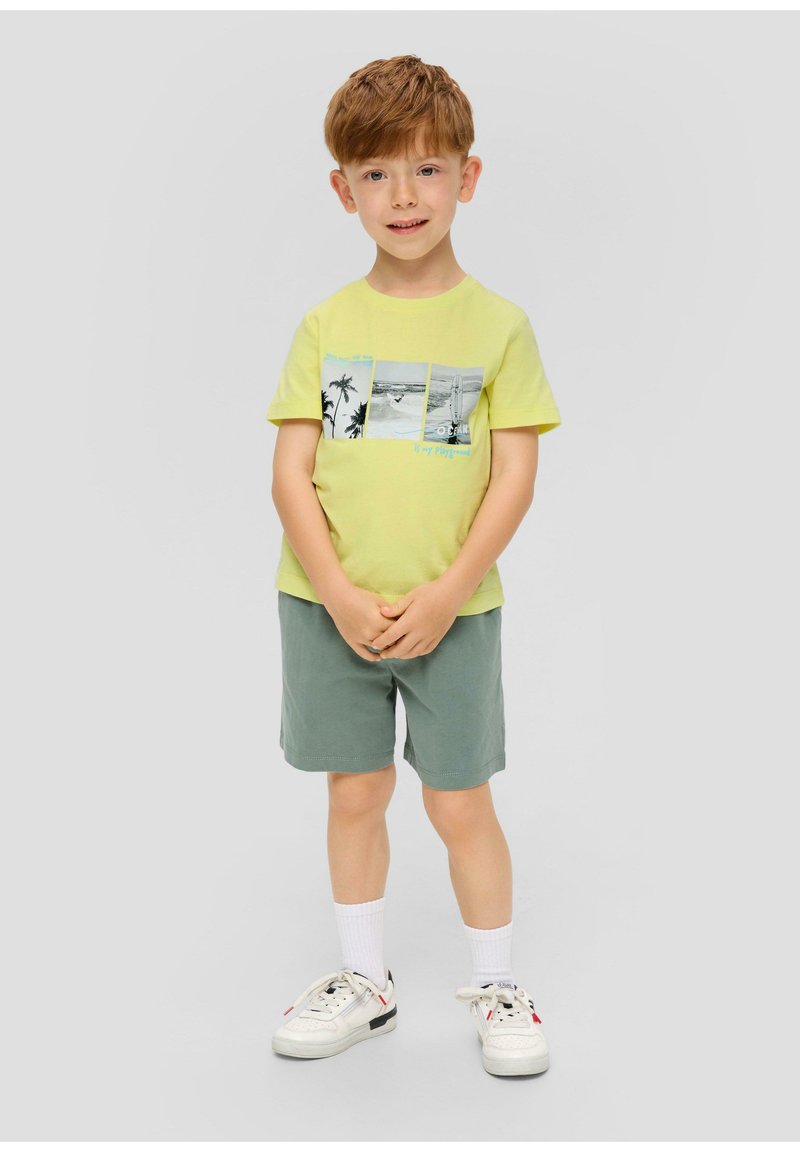 Geel katoenen t-shirt met grafische print en turkooise accenten, gecombineerd met groene shorts en witte sneakers met zwarte en rode details.