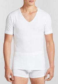Maglietta bianca a V in tessuto liscio, con maniche corte e un design aderente. Abbinata a slip bianchi.