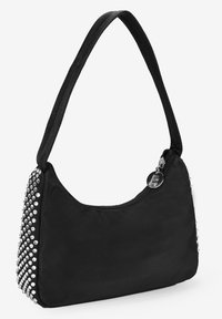 Bolso de mano negro de nailon, con forma redondeada, detalles de tachuelas en un lado y cierre con cremallera y tirador metálico.