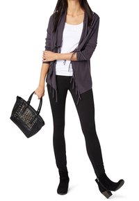 Mörkgrå öppen-front kofta med fransar, vit tanktop, svarta leggings och ankelboots. Svart handväska med nitar.