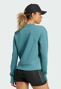 Turquoise sweatshirt with a crew neck and raglan sleeves, paired with black shorts featuring three dark stripes on the side.