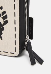 Pochette nera e crema con texture, caratterizzata da un design grafico audace, dotata di una chiusura con zip argentata e un'etichetta con logo, accentuata da cuciture nere.