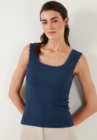 Tume sinine sobiv tank top, mis on valmistatud tekstuuriga kangast ning millel on laineline pitsääris kaeluse ja käeaukude ümber.