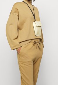 Beige Sweatshirt mit hohem Kragen, lockerer Passform und gerippten Bündchen, kombiniert mit passenden Jogginghosen und einer kleinen crema-farbenen Umhängetasche.