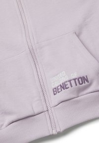 Felpa con zip di un leggero colore viola, realizzata in tessuto morbido. Presenta polsini e orlo a coste, con "United Colors of Benetton" ricamato sul davanti.