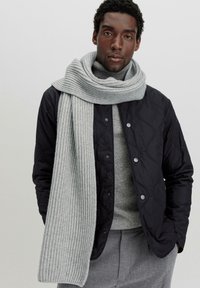 Schwarze gesteppte Jacke, hellgrauer gerippter Schal, grauer Pullover, graue Hose. Glatte Textur, Knopfdetails an der Jacke, warme Schichten.