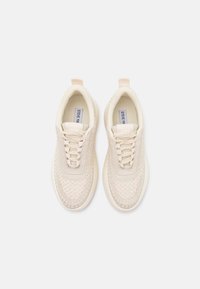 Beige sneakers med en struktureret strikket overdel og glatte detaljer. Har snørebåndsdesign og en løkkerem bagpå. Gummiydersål.