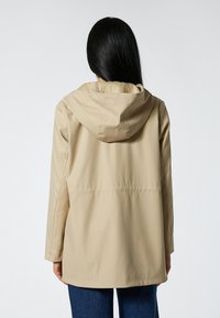Beige waterdichte jas met een capuchon, met een rechte snit en zichtbare stiksels. Gemaakt van glad, lichtgewicht materiaal.