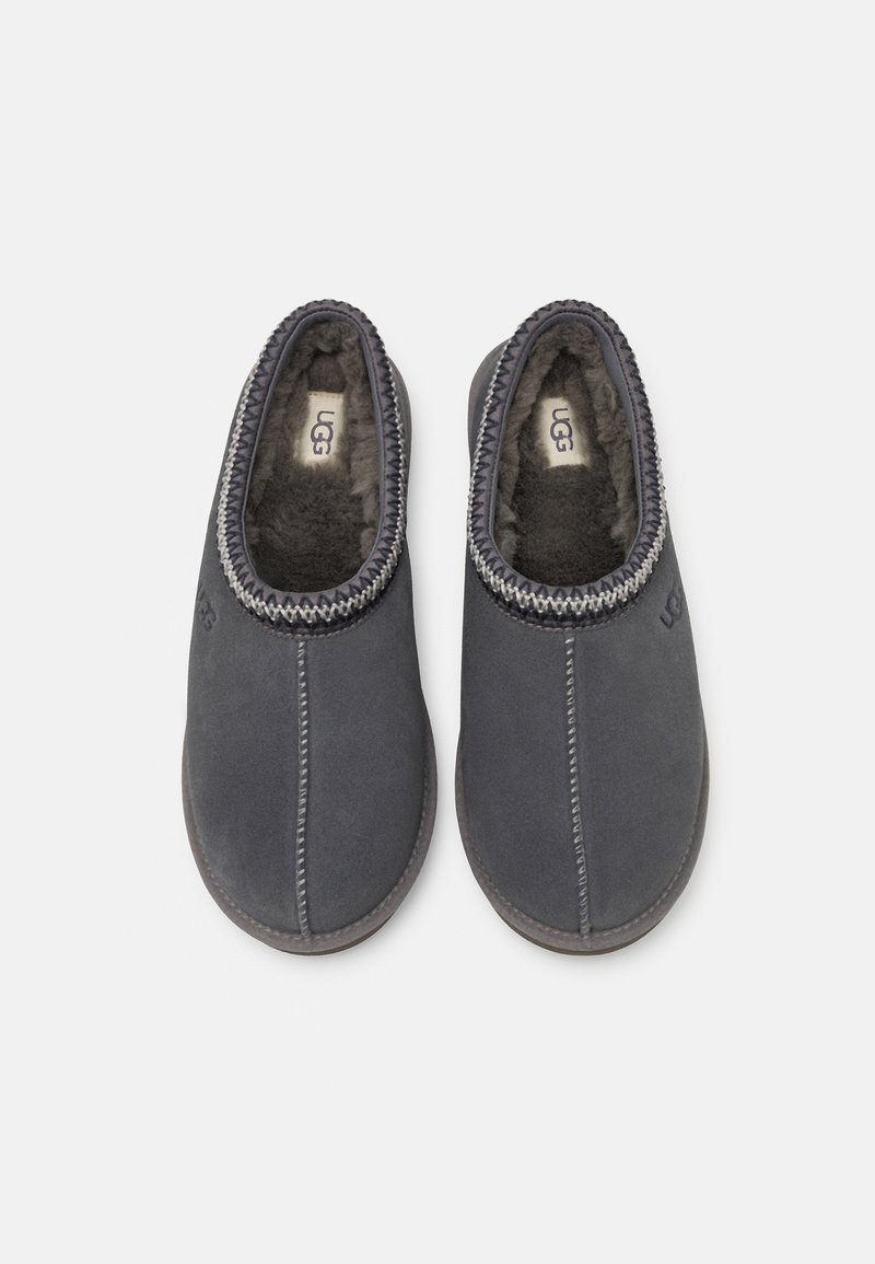 Graue Wildlederschuhe mit einem weichen Futter aus Fell, elastischem Einstieg und kontrastierenden Nähten. Mit UGG-Branding auf der Seite.