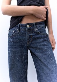 Tummansiniset farkut kuluneella tekstuurilla, joissa on nappikiinnitys, etutaskut ja hillitty haalistumakuosi.