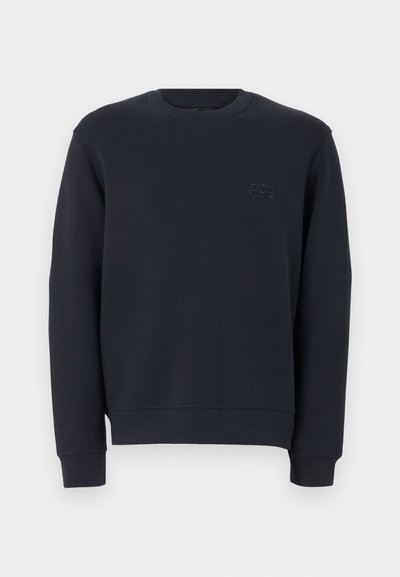 Σκούρο μπλε φούτερ με στρογγυλή λαιμόκοψη, μακριά μανίκια και μικρό κεντημένο λογότυπο στο αριστερό στήθος, παρουσιάζεται σε λευκό φόντο.