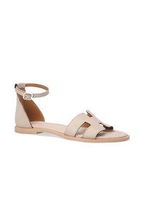 Beige Leder-Sandale mit einem Knöchelriemen, offener Zehenpartie, zwei Ausschnitten im Obermaterial und einer flachen Holzsohle. Glatte Textur, minimalistisches Design.