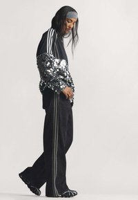 Čierny športový top so trblietavými striebornými flitrovými rukávmi, v kombinácii s čiernymi širokými nohavicami s vertikálnymi pruhovanými akcentmi.