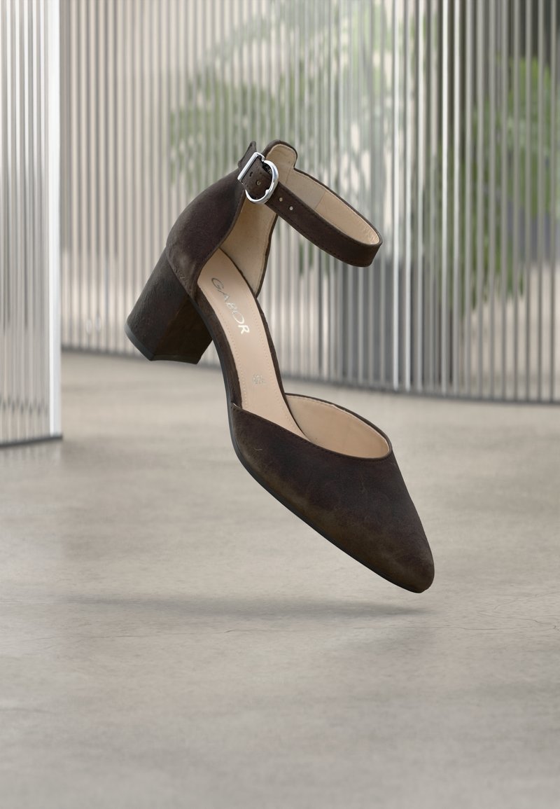 Chaussure à talon en daim marron avec une bride à la cheville, un bout pointu et un talon carré. La semelle est lisse et l'intérieur est de couleur crème.