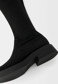 Svarta ankelstövlar i mocka med en tjock, strukturerad gummisula, elastiska sidopaneler och en slät, rundad design.