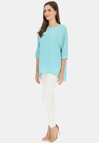 Luźna, jasnoniebieska bluzka z dekoltem łódkowym i rękawami o długości trzy czwarte, zestawiona z białymi, dopasowanymi dżinsami i beżowymi szpilkami.